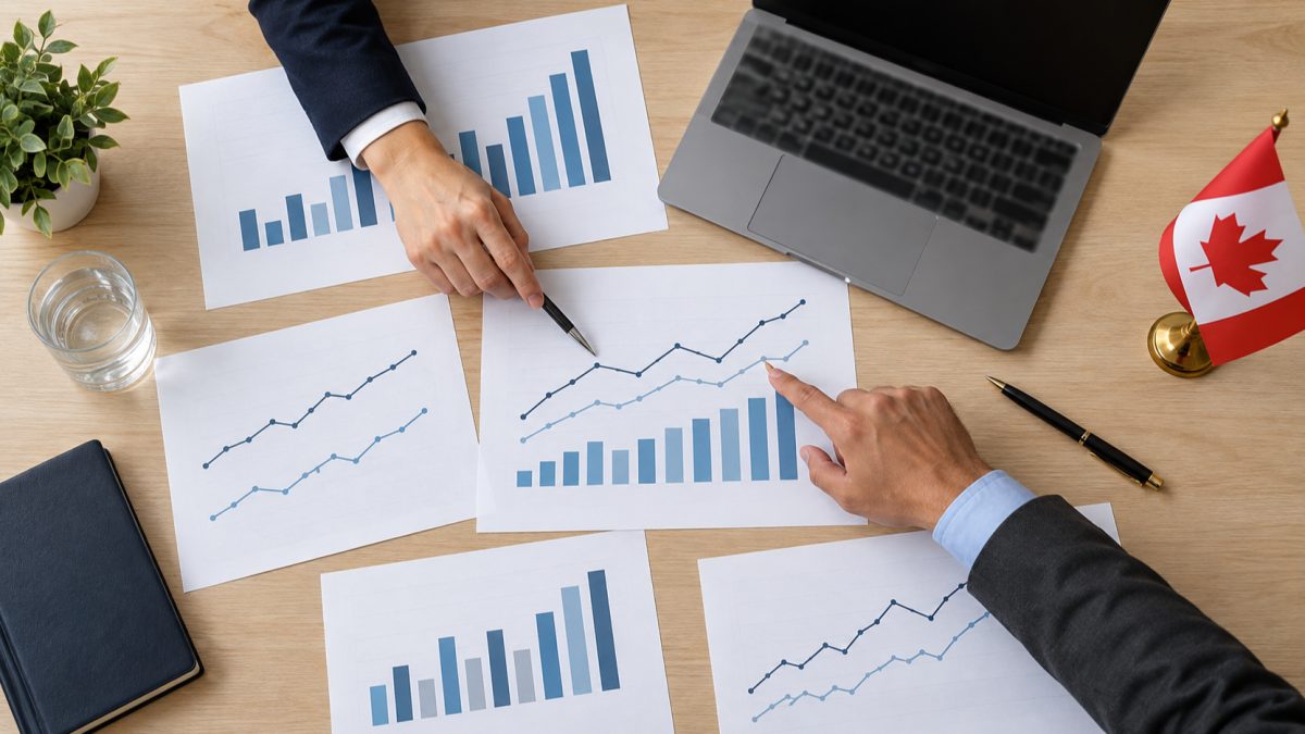 Two people reviewing printed charts on a meeting table beside a laptop and a small Canadian flag.